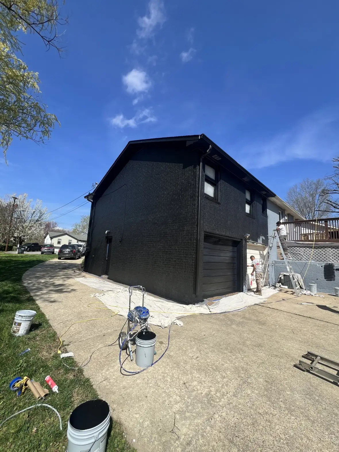 Drop Zone Painting exterior repaint in progress — spray rig and freshly painted home